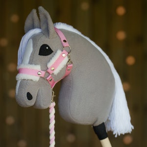 May include: A gray and white stuffed horse head with a pink bridle and white mane. The horse is attached to a wooden stick.