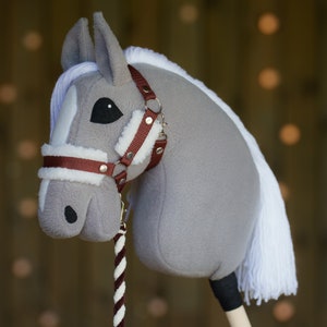 May include: A gray and white plush rocking horse with a brown leather bridle and reins. The horse has a white mane and tail.