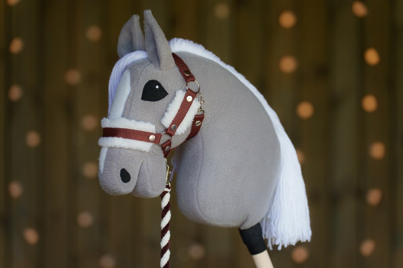 May include: A gray and white plush rocking horse with a brown leather bridle and reins. The horse has a white mane and tail.