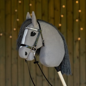 May include: A grey stuffed horse head with a black leather bridle and a silver and black beaded browband. The horse has a black mane and tail.