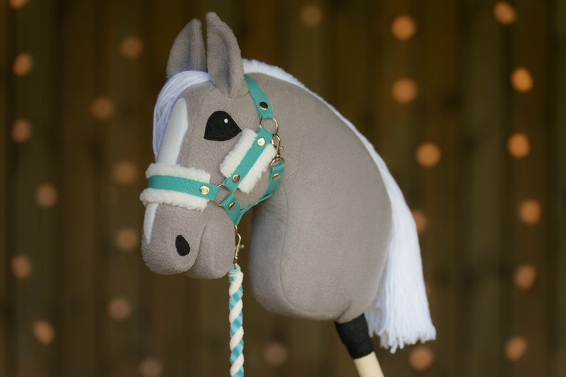 May include: A gray and white stuffed horse head with a turquoise and gold bridle. The horse has a white mane and tail.