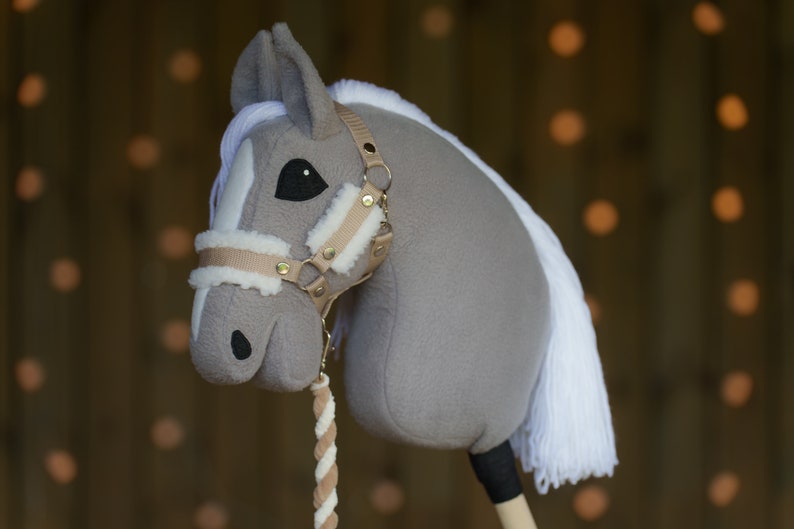 May include: A gray and white plush rocking horse with a brown leather halter and reins. The horse has a white mane and tail.