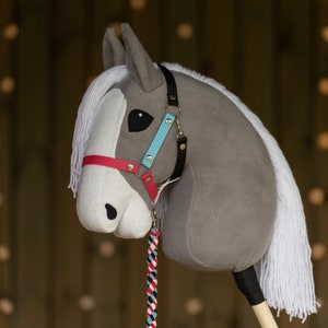 May include: A gray and white plush horse head with a red, blue, and white bridle. The horse has a white mane and tail.
