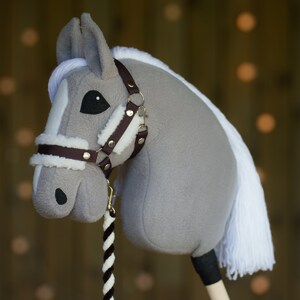 May include: A gray and white rocking horse with a brown leather bridle and a white mane and tail. The horse is standing on a wooden base.