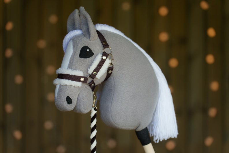 May include: A gray and white rocking horse with a brown leather bridle and a white mane and tail. The horse is standing on a wooden base.