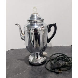 May include: A vintage electric percolator coffee pot made of polished chrome with a black handle and a clear glass knob on the lid. The coffee maker features a tall, urn-shaped body, a curved spout, and comes with a black electrical power cord.