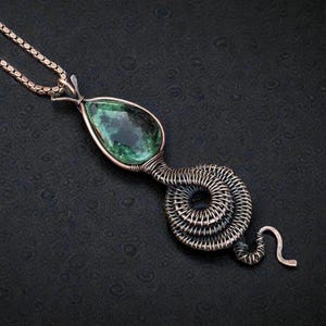 May include: A handcrafted copper pendant necklace featuring a teardrop-shaped green gemstone. The gemstone is encased in a copper wire frame, with a coiled wire design and a chain. The pendant has a unique, artistic design.