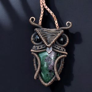 May include: A handcrafted copper wire owl pendant with a green and purple stone center and black bead eyes. The pendant is suspended from a copper chain, showcasing intricate wire wrapping and a unique, artistic design. The owl pendant is a statement piece.