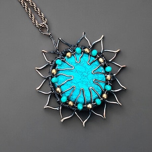 May include: A handcrafted pendant necklace featuring a turquoise stone center, surrounded by a wire-wrapped design. The pendant has a sunburst shape with silver-toned metal and turquoise beads. The necklace chain is a twisted rope style.