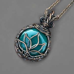 May include: A handcrafted pendant necklace featuring a teal-colored, oval-shaped stone with a copper wire lotus design. The stone is encased in a wire-wrapped setting with a bronze-colored chain. The pendant is approximately 1.5 inches in length.