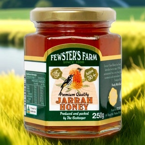 May include: A glass jar of Jarrah honey from Fewster's Farm, a family-owned business since 1898. The jar is labeled with a green and gold design featuring a bird and a flower. The honey is 250g and is described as "Premium Quality".