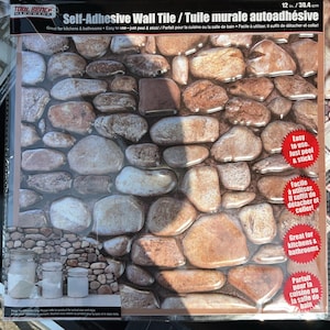 May include: Self-adhesive wall tile featuring a stone pattern. The tile is 12 inches (30.4 cm) wide and designed for kitchens and bathrooms. The packaging includes the text "Easy to use. Just peel & stick!"