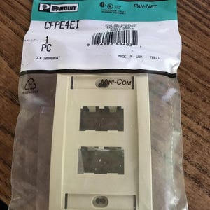 May include: A beige Mini-Com faceplate in a clear plastic bag. The faceplate has two rectangular openings and a lower oval opening. The bag has the Panduit and Pan-Net logos, along with the text "CFPE4EI" and "Mini-Com".