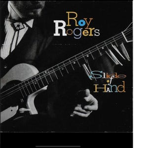 May include: Album cover for "Slide of Hand" by Roy Rogers. The image features a black background with the artist's name in white and yellow text. A guitar is prominently displayed, with the artist's hand pointing towards the viewer.