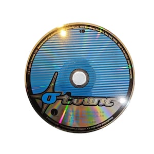 May include: A CD with a blue and silver design. The center has a blue circle with a white center. The CD has the word "O-Town" in silver and black. The CD also has text that includes the words "J Records LLC" and "Made in the U.S.A."