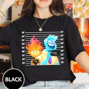 May include: Black t-shirt featuring a cartoon illustration of two characters, one with blue skin and the other with orange flames, standing in a police lineup. The text "LAPD AND WADE" is visible on the blue character's badge.
