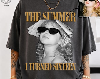 May include: A charcoal grey crewneck t-shirt featuring a black and white photographic print of a child wearing sunglasses and a newspaper hat. The text reads THE SUMMER I TURNED SIXTEEN and Emily. A small inset box shows the original photo reference.