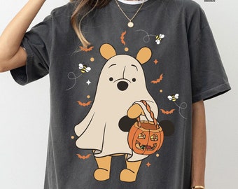 Op de afbeelding: Donkergrijs T-shirt met een cartoon spookfiguur met een pompoenmand, omringd door bijen, vleermuizen en sterren. Het shirt heeft de tekst "PEPPER COMFORT COLORS" in een cirkel.