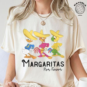 May include: A white t-shirt with a graphic of three cartoon characters wearing sombreros. The characters are a duck, a rooster, and a parrot. The text "Margaritas Por Favor" is printed below the characters.