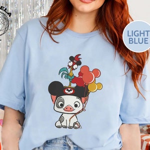 May include: Light blue t-shirt featuring a cartoon pig wearing Mickey Mouse ears and holding balloons. A rooster with a red comb is perched on top of the pig's head.