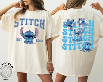 May include: A white t-shirt with a blue Stitch graphic on the front and a blue Stitch graphic with the text "Stitch" repeated on the back. The text on the front reads "Stitch Est 2002".
