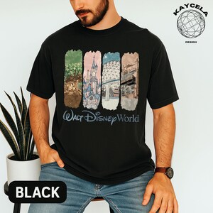 Op de afbeelding: Zwart t-shirt met een kleurrijke afbeelding van bezienswaardigheden van Walt Disney World. Het ontwerp bevat afbeeldingen van een kasteel, Spaceship Earth en andere attracties. De woorden "Walt Disney World" staan eronder in een scriptletter.