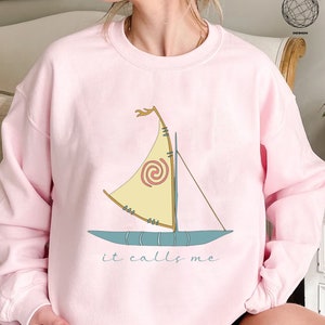 May include: Pink sweatshirt with a cartoon image of a sailboat and the text "it calls me".