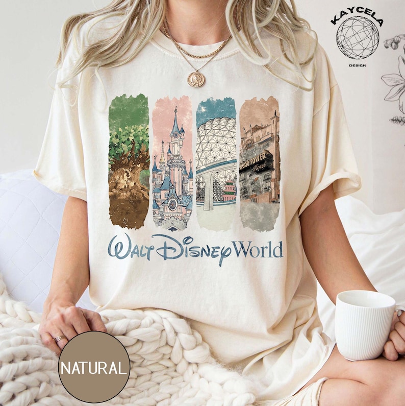 Op de afbeelding: Cr&egrave;mekleurig T-shirt met een kleurrijke afbeelding van Walt Disney World-bezienswaardigheden. Het ontwerp bevat illustraties van een kasteel, Spaceship Earth en andere attracties. De woorden "Walt Disney World" zijn in blauwe letters gedrukt.