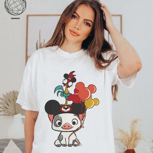 May include: White t-shirt featuring a cartoon image of a pig wearing Mickey Mouse ears. The pig is holding a rooster with red, yellow and blue balloons.