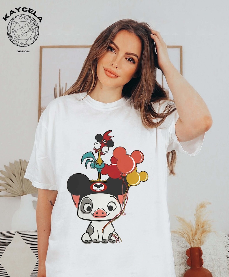 May include: White t-shirt featuring a cartoon image of a pig wearing Mickey Mouse ears. The pig is holding a rooster with red, yellow and blue balloons.