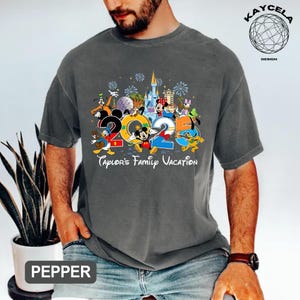 Puede incluir: Camiseta gris con un gr&aacute;fico colorido que presenta personajes de Disney y el a&ntilde;o "2025". El texto "Taylor's Family Vacation" est&aacute; debajo. La camiseta tiene cuello redondo y mangas cortas.