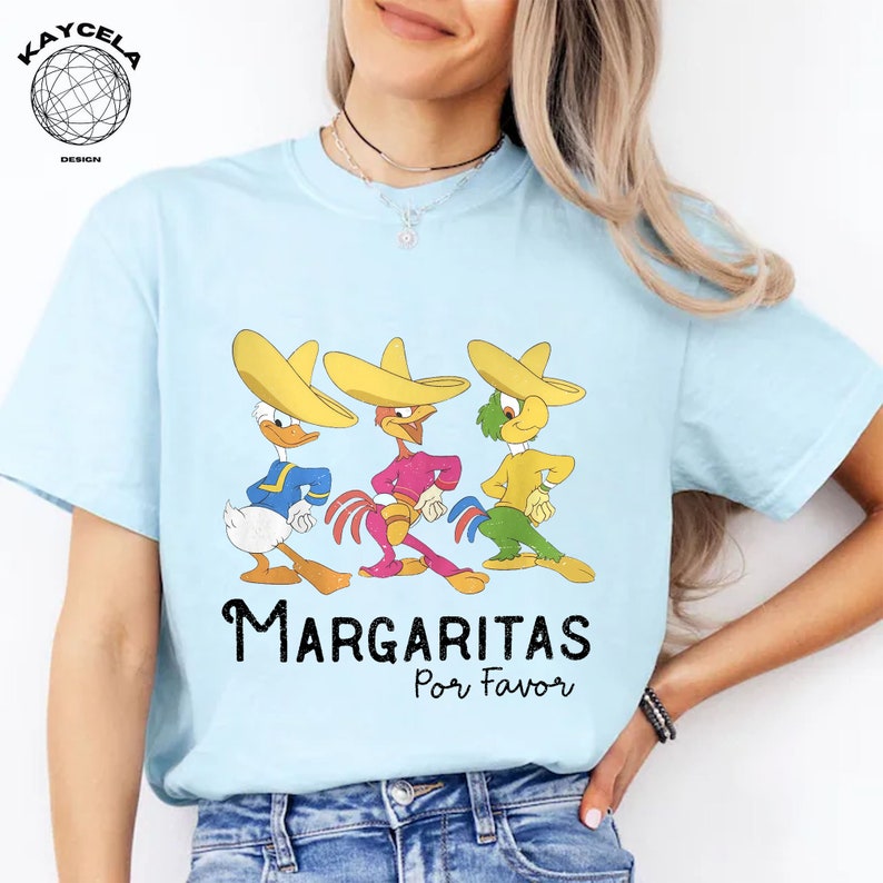 May include: A light blue t-shirt with a graphic of three cartoon characters wearing sombreros. The characters are a duck, a rooster, and a parrot. The text "Margaritas Por Favor" is printed below the characters.
