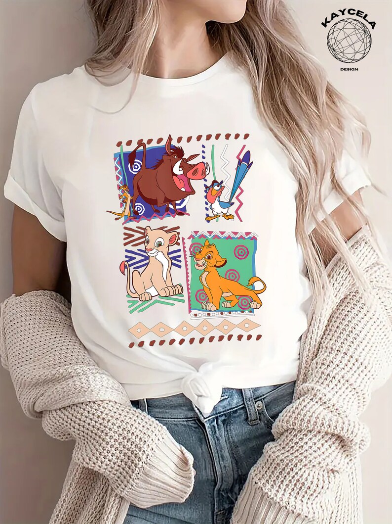 May include: White t-shirt with a colorful graphic print of characters from the movie The Lion King. The characters include Simba, Nala, Pumbaa, and Zazu. The graphic is surrounded by a colorful geometric pattern.