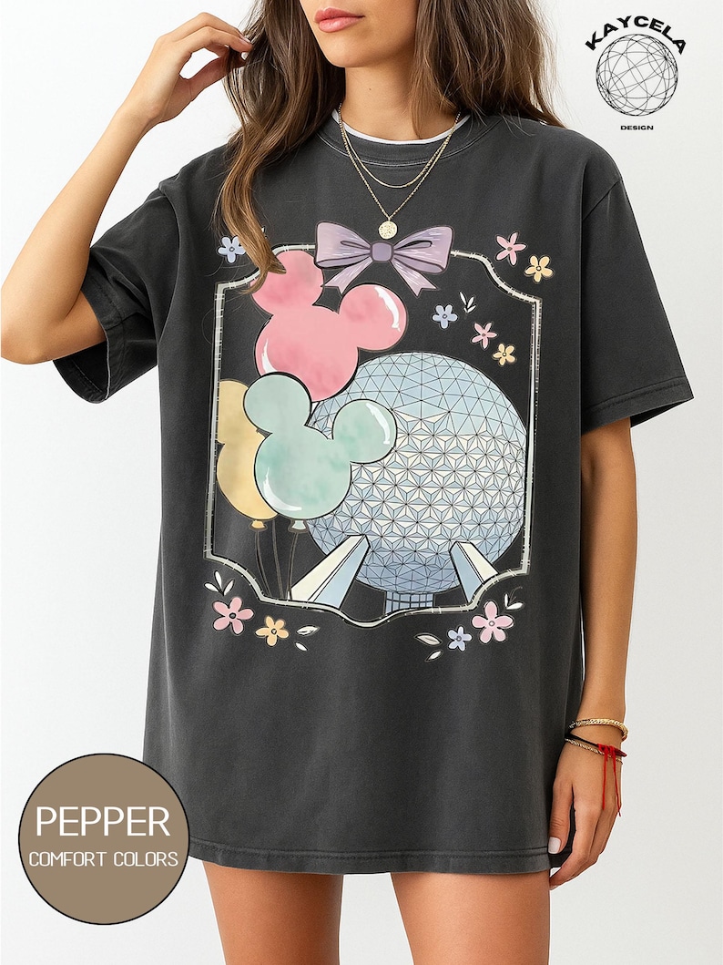 May include: Dark gray t-shirt featuring a graphic of Mickey Mouse balloons, a bow, and a geometric sphere. The design includes pastel pink, blue, and yellow colors. The shirt has the text "PEPPER COMFORT COLORS" at the bottom.
