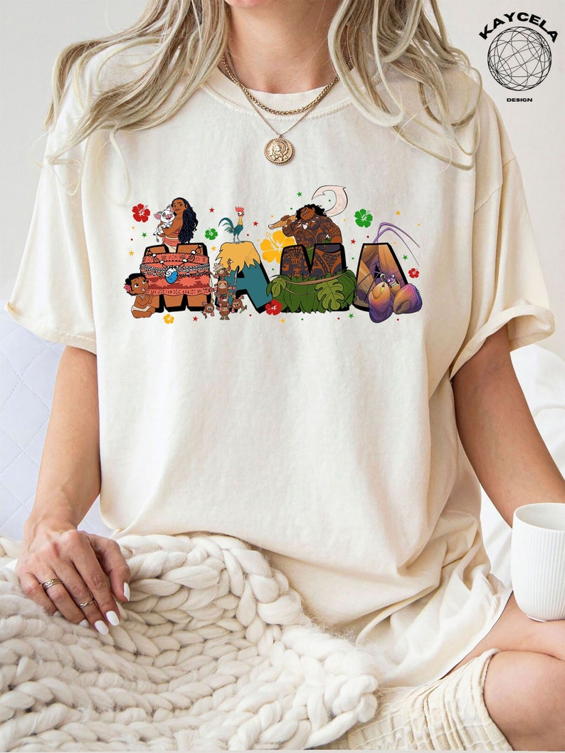 K&ouml;nnte beinhalten: Ein wei&szlig;es T-Shirt mit einer bunten Grafik von Figuren aus dem Film Vaiana. Die Grafik lautet "MAMA" mit den Figuren aus dem Film, die die Buchstaben umgeben.