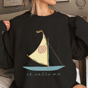 May include: Black sweatshirt with a cartoon image of a sailboat with a spiral design and the text "it calls me".