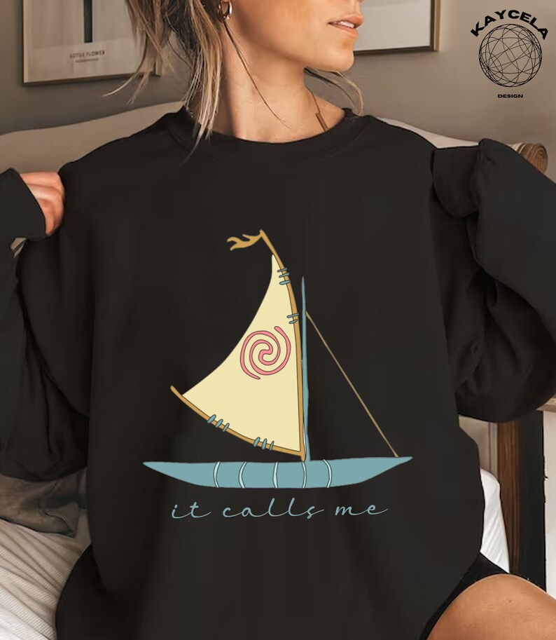 May include: Black sweatshirt with a cartoon image of a sailboat with a spiral design and the text "it calls me".