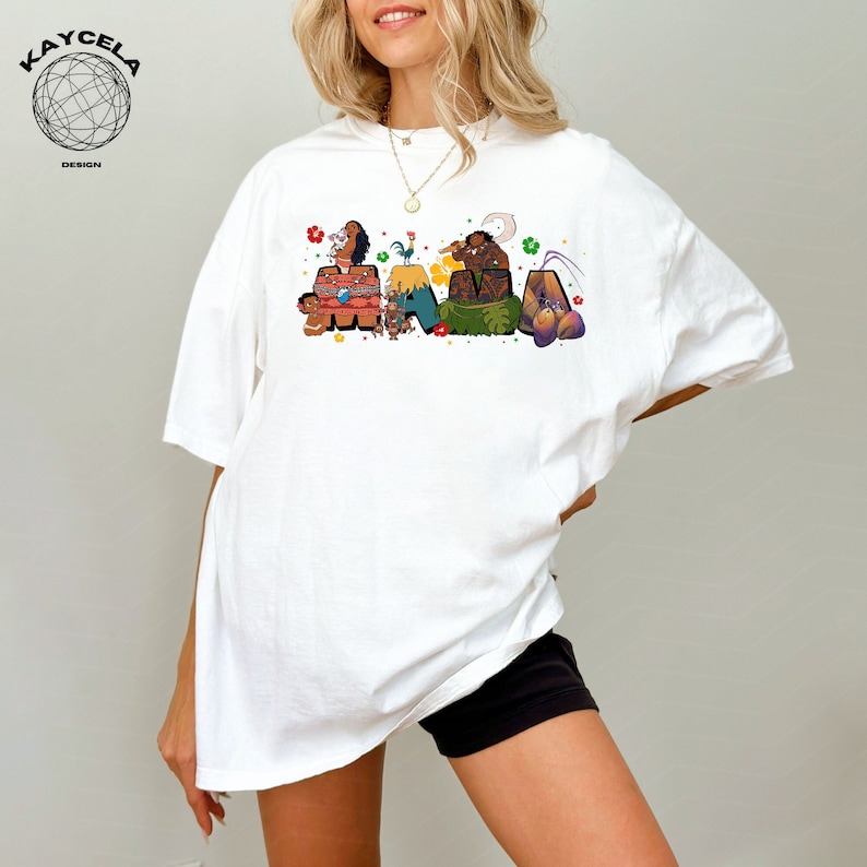 K&ouml;nnte beinhalten: Wei&szlig;es T-Shirt mit einer bunten Grafik von Figuren aus dem Film Vaiana, die "Mama" buchstabieren.