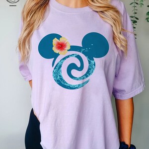 May include: A lavender t-shirt with a blue Mickey Mouse silhouette featuring a wave design and a pink hibiscus flower.