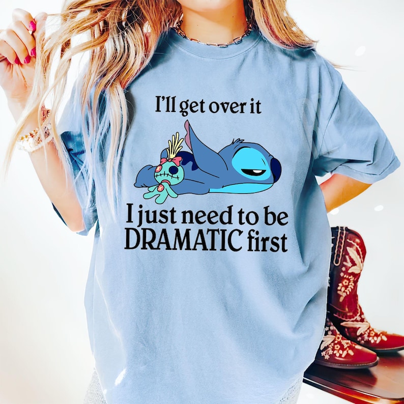 May include: Light blue t-shirt with a cartoon Stitch character from Lilo & Stitch. The text on the shirt reads "I'll get over it I just need to be DRAMATIC first."