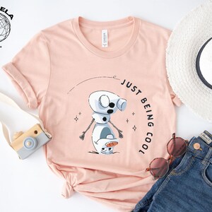 May include: A pink t-shirt with a cartoon snowman graphic and the text "Just Being Cool".