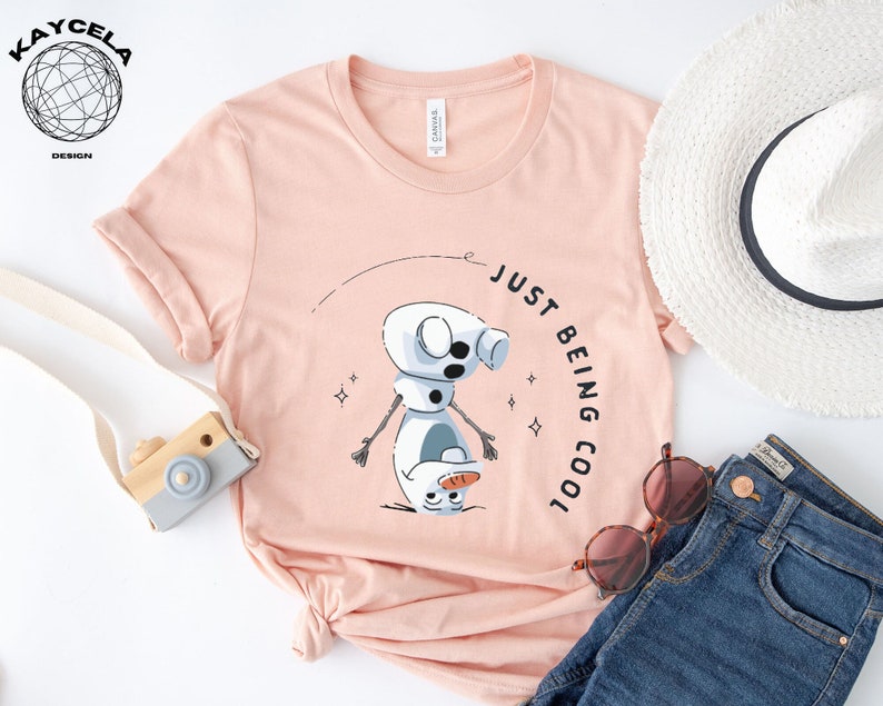May include: A pink t-shirt with a cartoon snowman graphic and the text "Just Being Cool".
