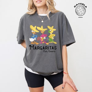 May include: A gray t-shirt with a graphic of four cartoon characters wearing sombreros. The characters are a duck, a rooster, and two parrots. The text "Margaritas Por Favor" is printed below the characters.