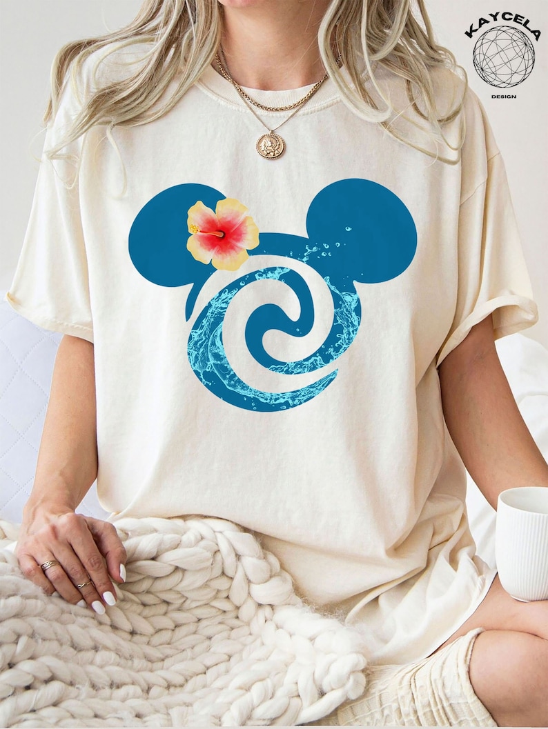 May include: A white t-shirt featuring a blue and white swirl design in the shape of Mickey Mouse ears. A yellow hibiscus flower is on top of one ear.