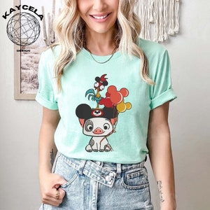 May include: A light blue t-shirt featuring a cartoon image of a pig wearing Mickey Mouse ears and holding balloons. A rooster is perched on top of the pig's head.
