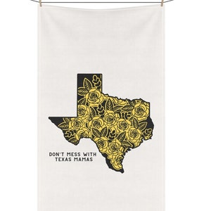 May include: White kitchen towel with a black outline of the state of Texas filled with yellow roses. The text "DON'T MESS WITH TEXAS MAMAS" is printed below the Texas outline. The towel is hanging from a clothesline.