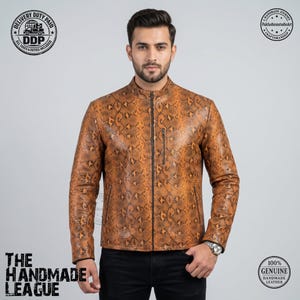 May include: A tan and black snakeskin-patterned leather jacket with a mandarin collar, a full-length front zipper, and a small vertical zippered chest pocket. The jacket features long sleeves and a straight hemline, worn over black trousers.