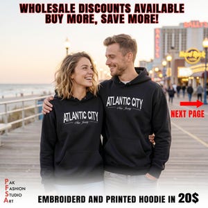 Puede incluir: Dos personas con sudaderas negras con "ATLANTIC CITY New Jersey" impreso en blanco. La imagen incluye el texto "WHOLESALE DISCOUNTS AVAILABLE BUY MORE, SAVE MORE!" y "EMBROIDERD AND PRINTED HOODIE".