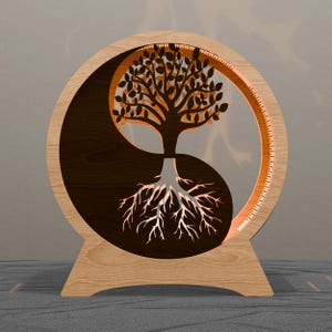 Könnte beinhalten: Ein hölzernes Yin-Yang-Symbol mit einem Baumdesign. Der Baum ist aus dem Holz geschnitten, mit den Wurzeln in der unteren Hälfte und den Ästen in der oberen Hälfte. Das Design wird von einem warmen Licht beleuchtet.