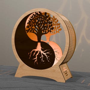 May include: A wooden Yin and Yang lamp featuring a tree design. The lamp has a circular frame with a cutout of a tree, its roots, and branches. The tree is split into two halves, one dark and one light, with an orange glow emanating from within.